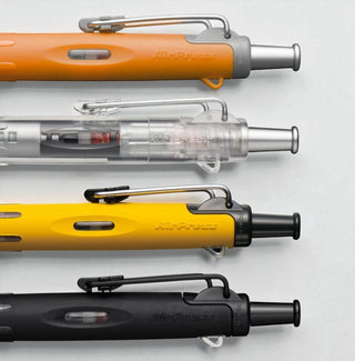 Close up of Tombow AirPress four pen set in different colors (orange, clear, yellow, black) on a light gray background - Shibuya Stationery Store
