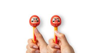 Two Funbox brand red colored Daruma Action Pen toppers with traditional Japanese designs held by hands against a white background - Shibuya Stationery Store