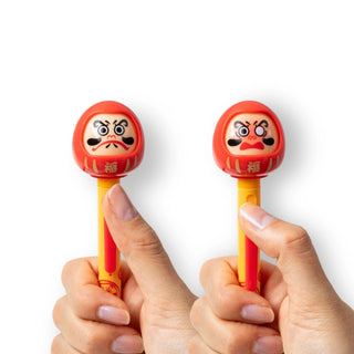 Two actions pens by Funbox Japanese stationery brand featuring red Daruma dolls with different faces being held side by side against a white background - Shibuya Stationery