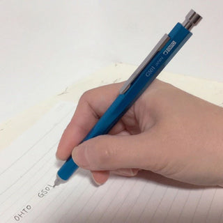 GS01 Needle Ballpoint Pen Blue held in hand while writing on paper – Shibuya Stationery