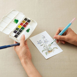 Person painting a floral design on paper with the Kuretake mini 14 watercolor paint and brush set - Shibuya Stationery Store