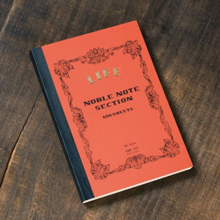 LIFE Noble Note notebook B6 grid in red placed on a wooden desk – Shibuya Stationery Store