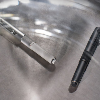 Uni-ball ZENTO Signature Model ballpoint pens in metallic black and silver placed on a gray table with white light and shadow - Shibuya Stationery Store